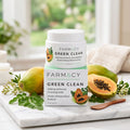 A jar of FARMACY GREEN CLEAN makeup meltaway cleansing balm is stacked on top of another jar and displayed on a marble tray with papayas, green leaves, and a wooden spoon in a bright, natural setting.