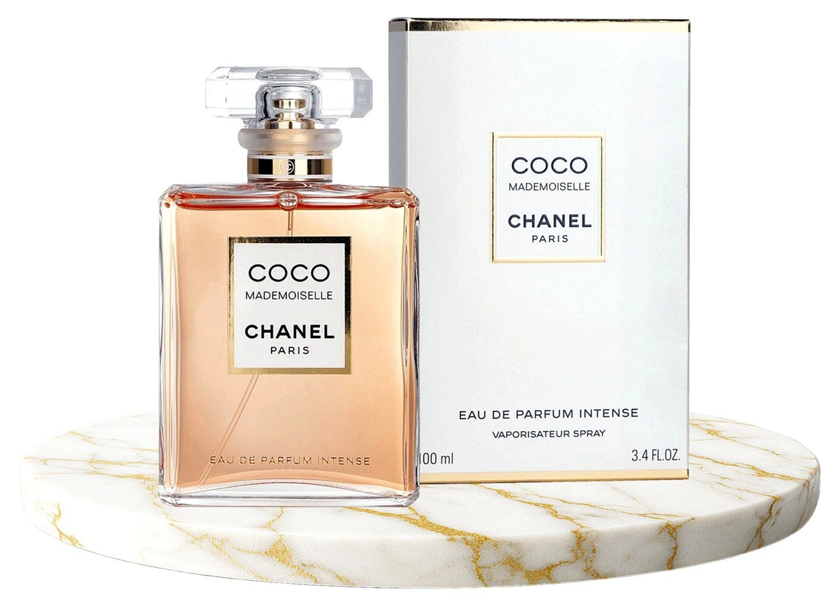 Chanel Coco Mademoiselle Eau de Parfum Intense 100ml bottle with its white packaging box, displayed on a round white marble pedestal against a white background.